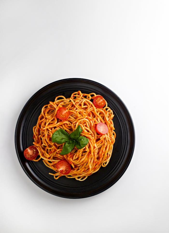 Delicious spaghetti with cherry tomatoes and basil on a black plate, shot from above.