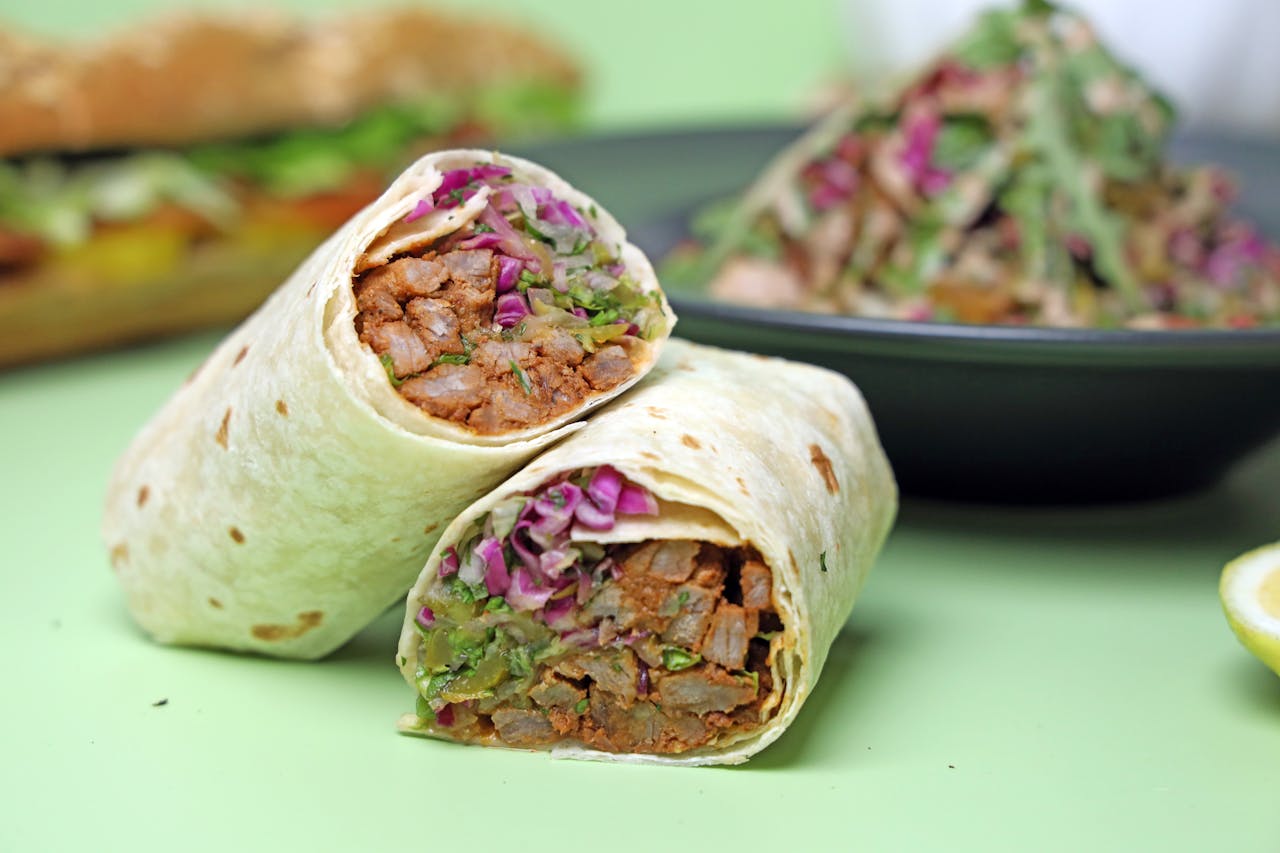 Tasty chicken wrap with fresh vegetables and a side salad on a light green background.