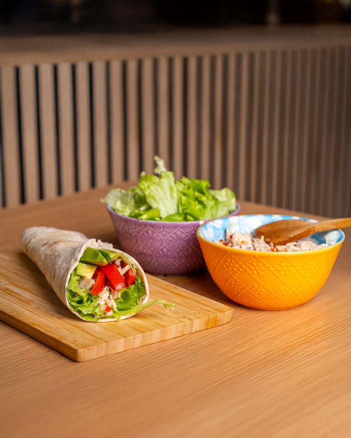 Delicious vegetarian wrap with fresh vegetables and salad in bowls on a wooden table.