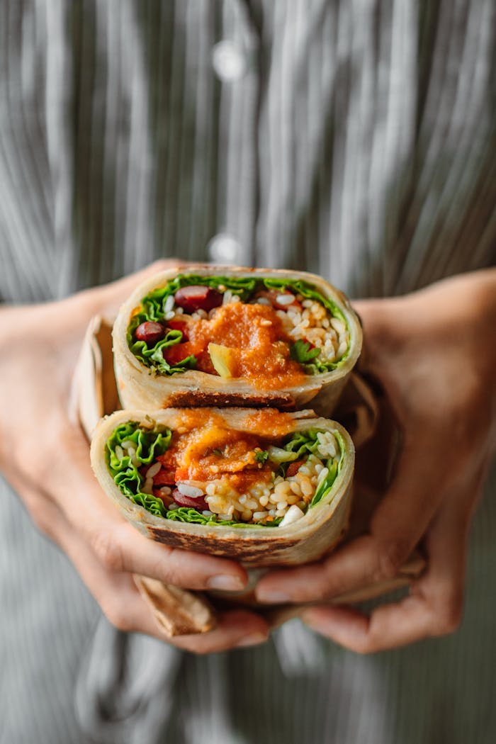 A close-up of hands holding a sliced vegetarian wrap with fresh vegetables and sauce.